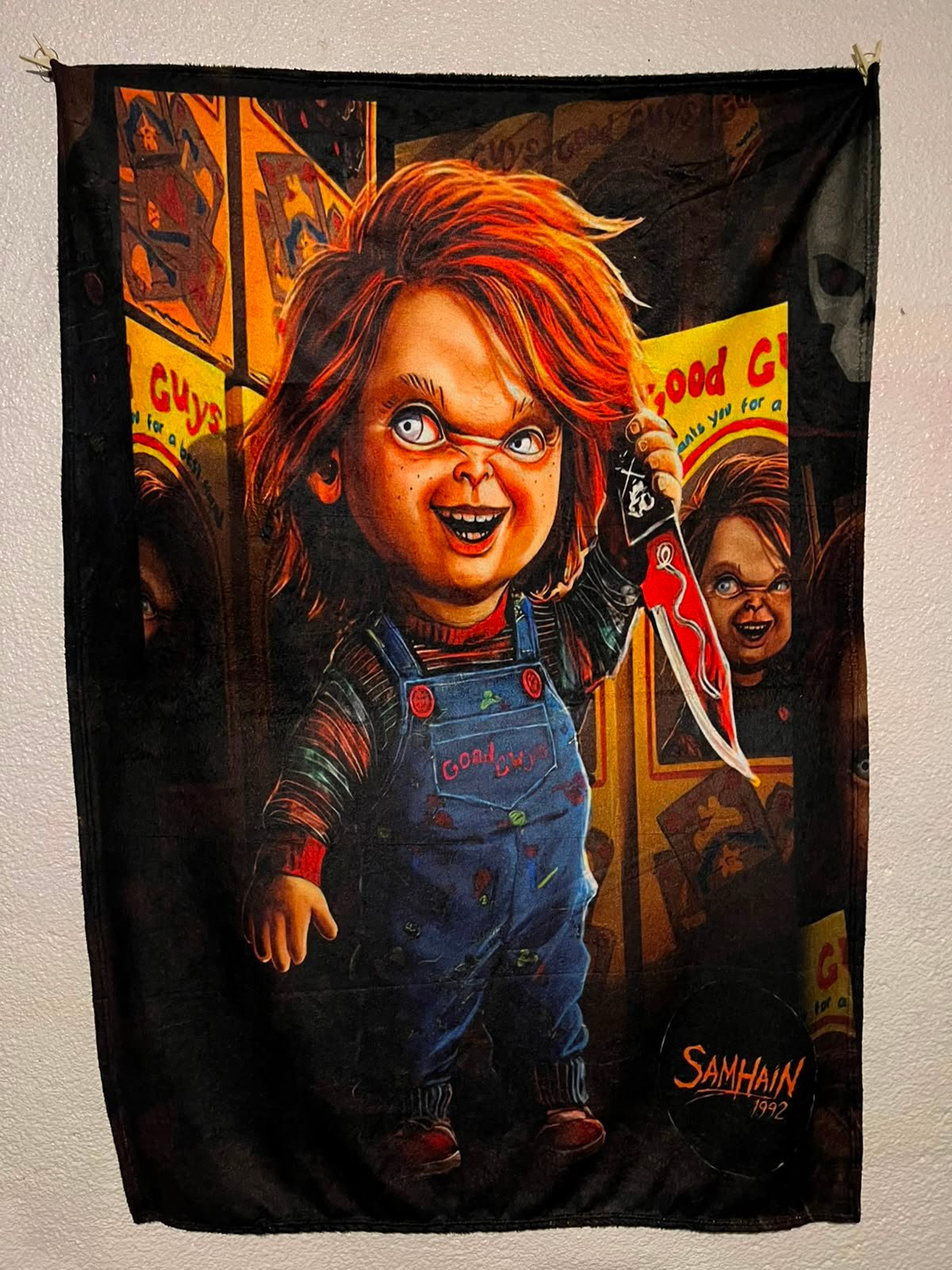 Frazada viajera de terror: Chucky con cuchillo frente a cajas de muñecos Good Guys